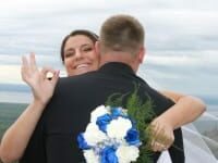 bride with blue and white bouquet making ok sign with hands while hugging groom