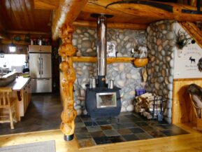 Fireplace surrounded by stone in cabin with kitchen and sitting room