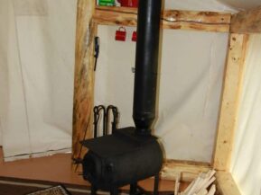 Wood stove in glamping cabin with bucket of wood nearby