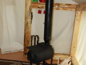 Wood stove in glamping cabin with bucket of wood nearby