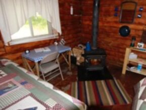 Wood stove and corners of bed in Bear's Den Cabin