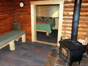 Woodburning stove and seating in Grub Steak Cabin with bedroom beyond