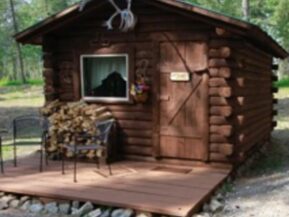 Exterior view of The Duke cabin with 2 chairs on porch and plenty of stacked wood