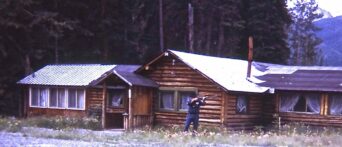 man holding rifle near log cabin
